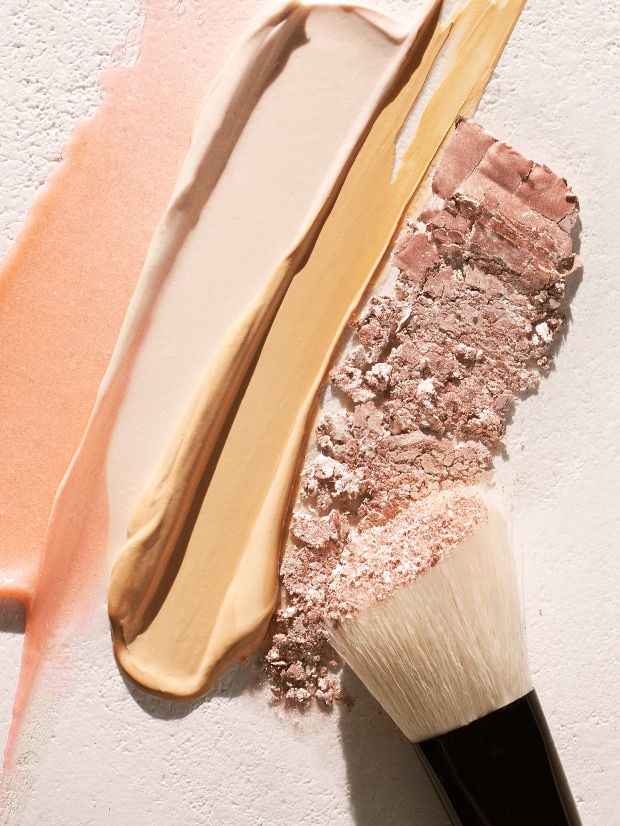 Close of of makeup brush over various makeup and skincare textures