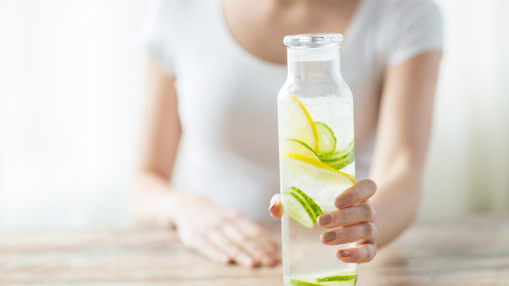 A woman holds a bottle of water with lemon and cucumber in it