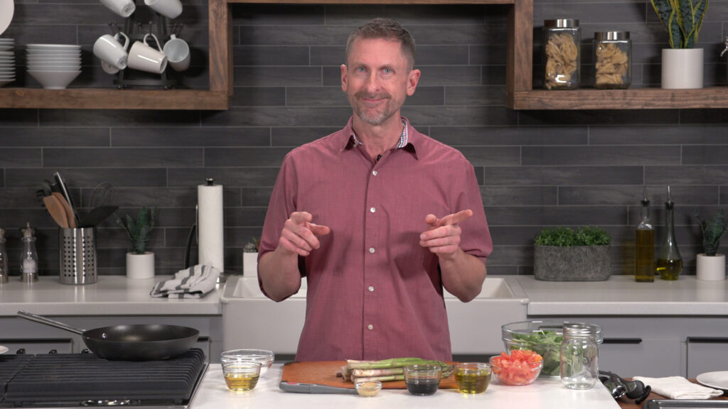 Chef Jeremy Reinicke stands in a kitchen with ingredients on a counter in front of him.