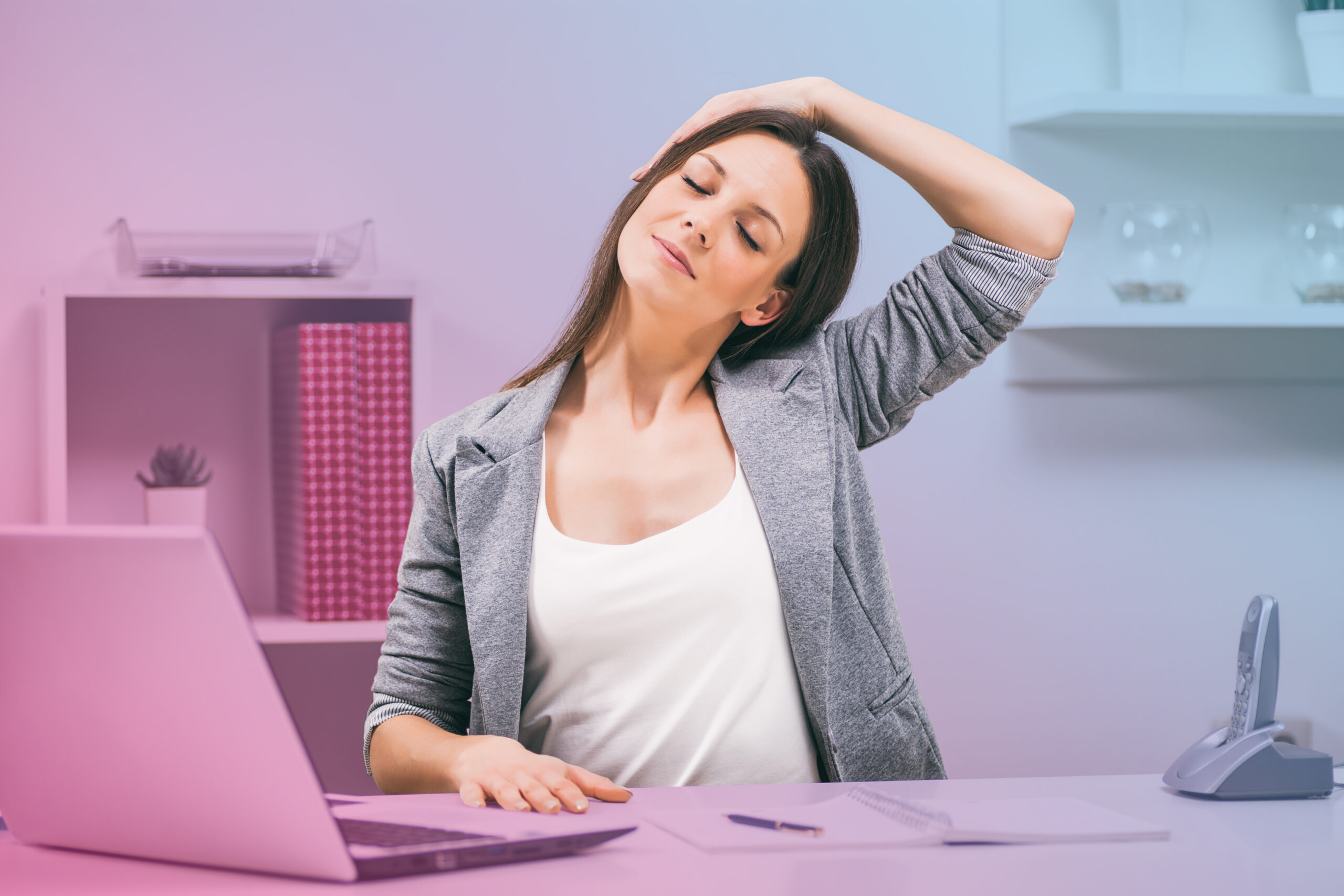 A woman stretches her neck in front of a computer